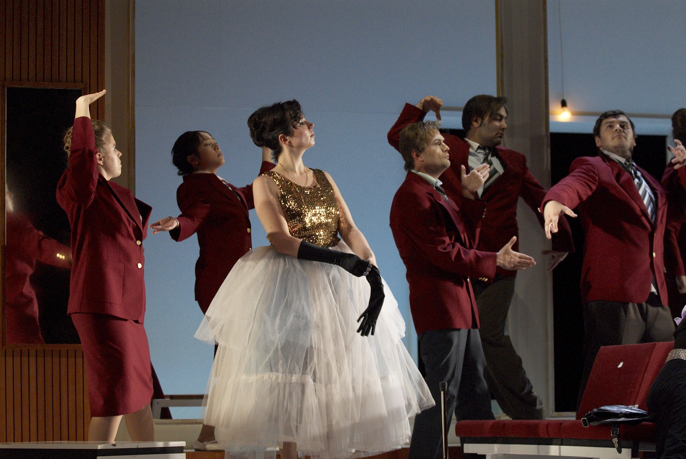 Stephanie Hampl in weißem Tüllrock vor tanzendem Ensemble in roten Sakkos bestehend aus Angelika Huber, Lusi Yang, Anton Leiss Huber, Sebastian Campione und Tobias Haaks