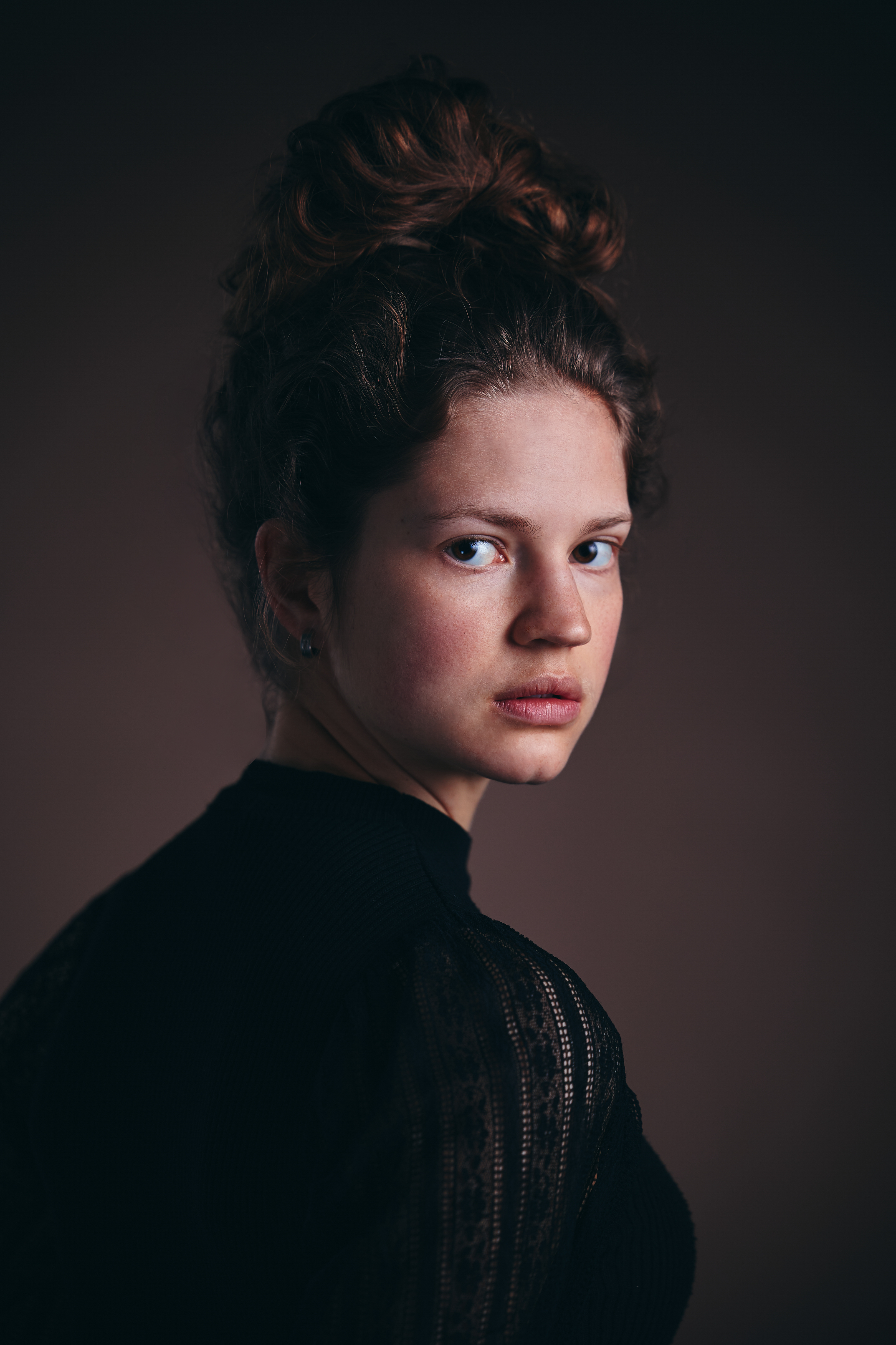 Portraitfoto von Sonja Reisenbichler: junge Frau mit hochgestecktem Haar und schwarzem Oberteil vor dunklem Hintergrund