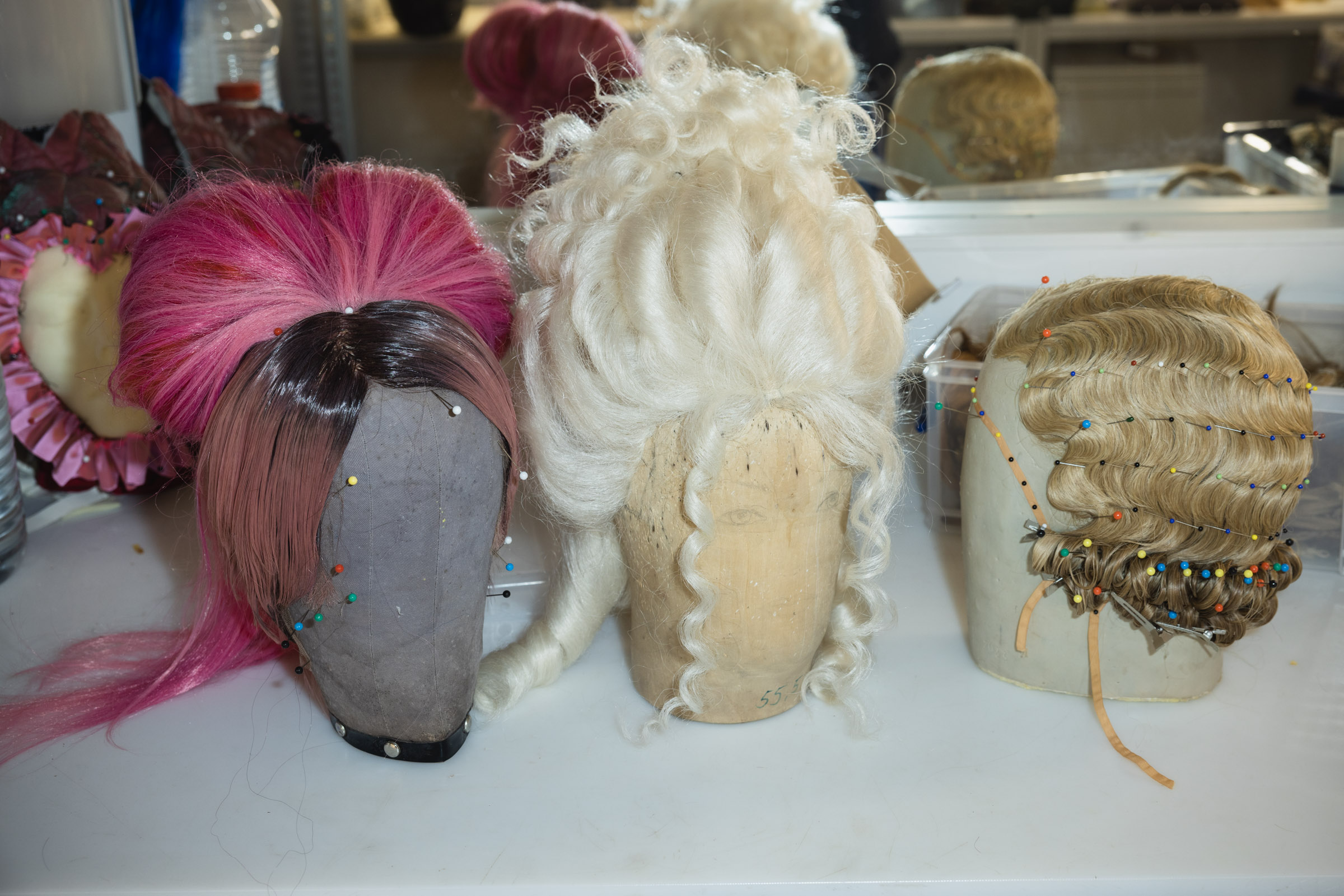 drei historisch frisierte Perücken (rosa, weiß, blond)
