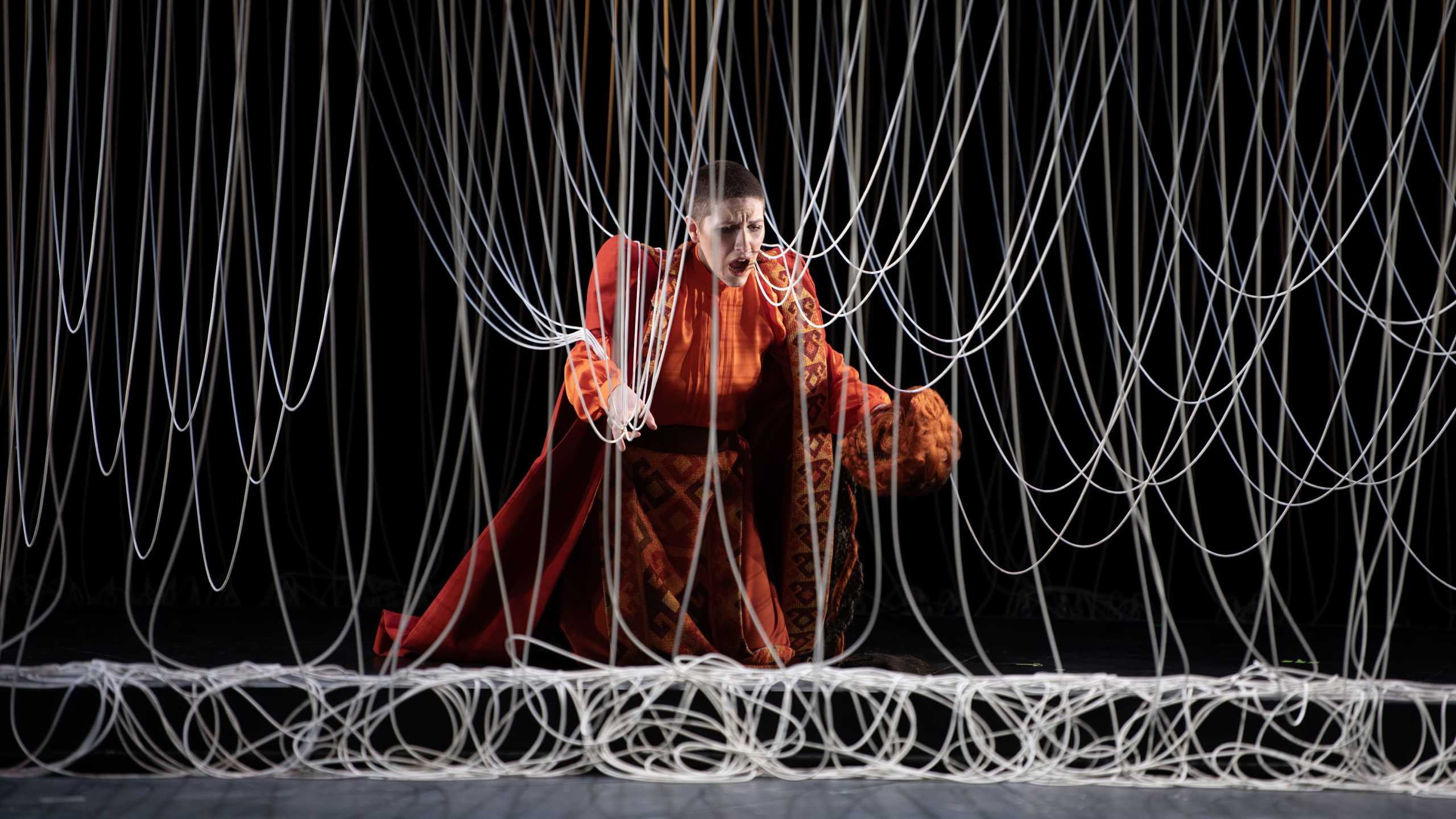 Mezzosopranistin Tamara Obermayer verkörpert die Rolle der Roselane in Johann Christian Bachs Zanaida. Sie steht im Roten Rüschenkleid zwischen zahlreichen Schnüren.