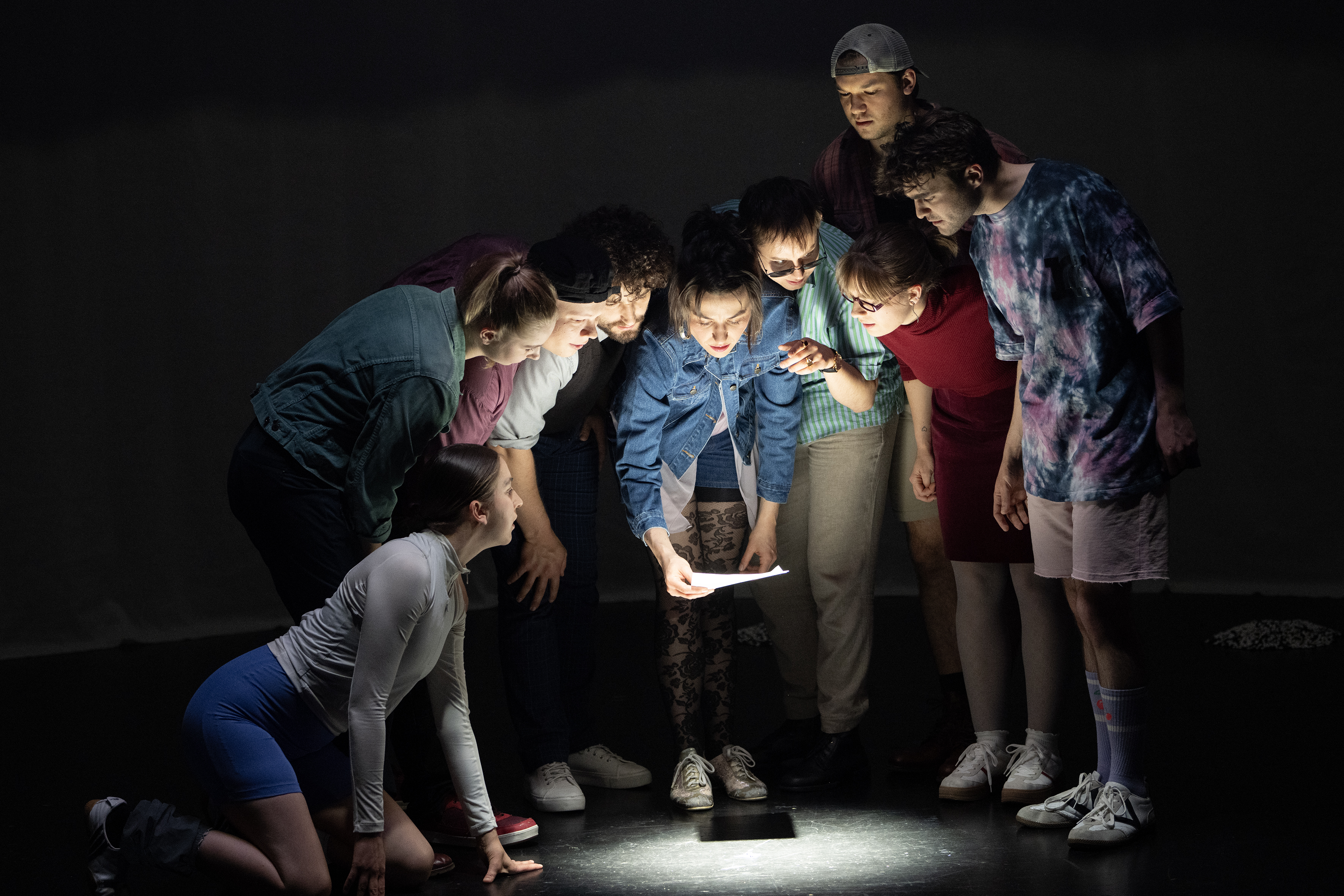 Szenenfoto: Gruppe von jungen Schauspielenden sehen auf Lichtkegel