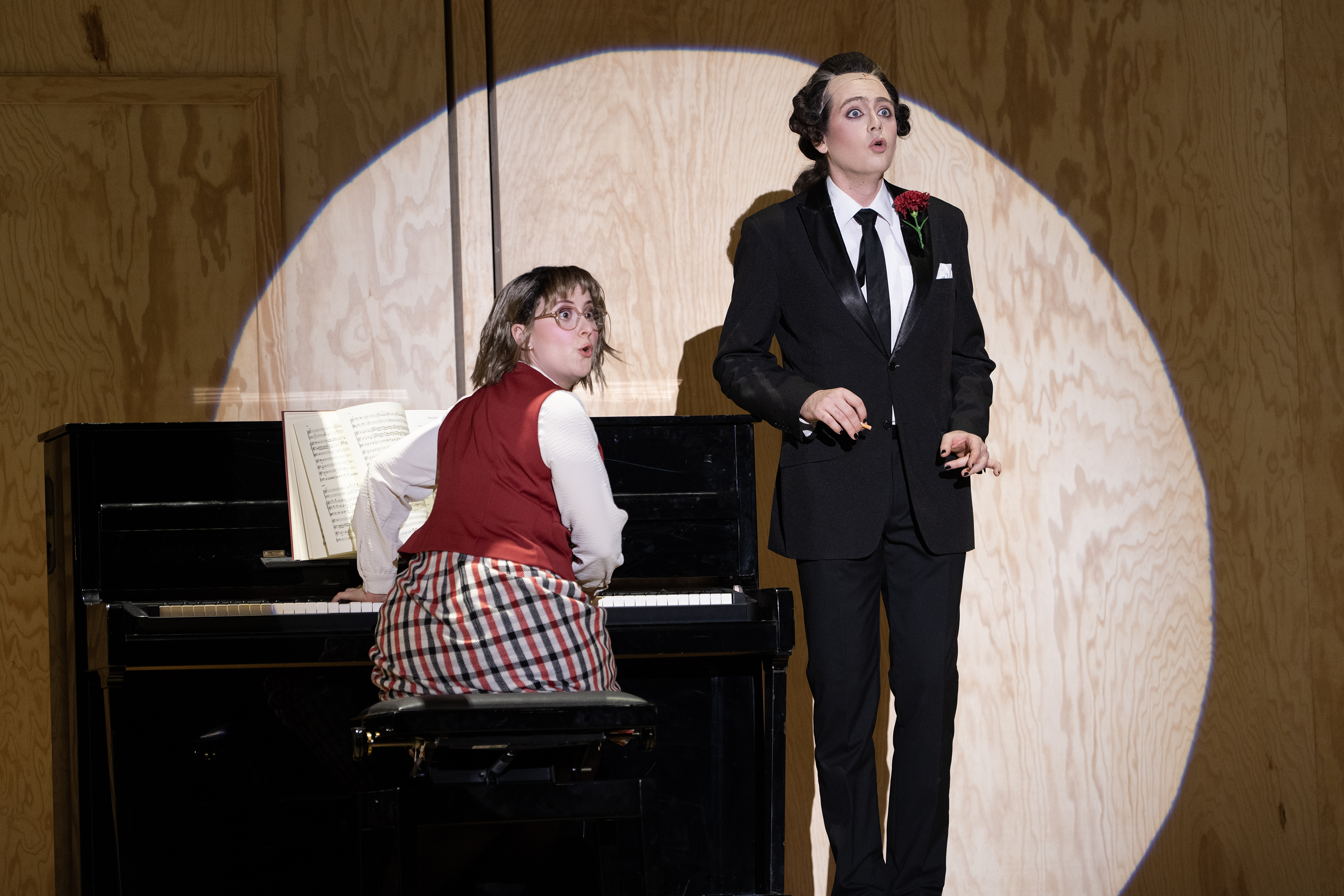 Eine Frau sitzt am Klavier, daneben ein Mann, beide schauen mit weit aufgerissenen Augen etwas an, sie sehen erstaunt aus