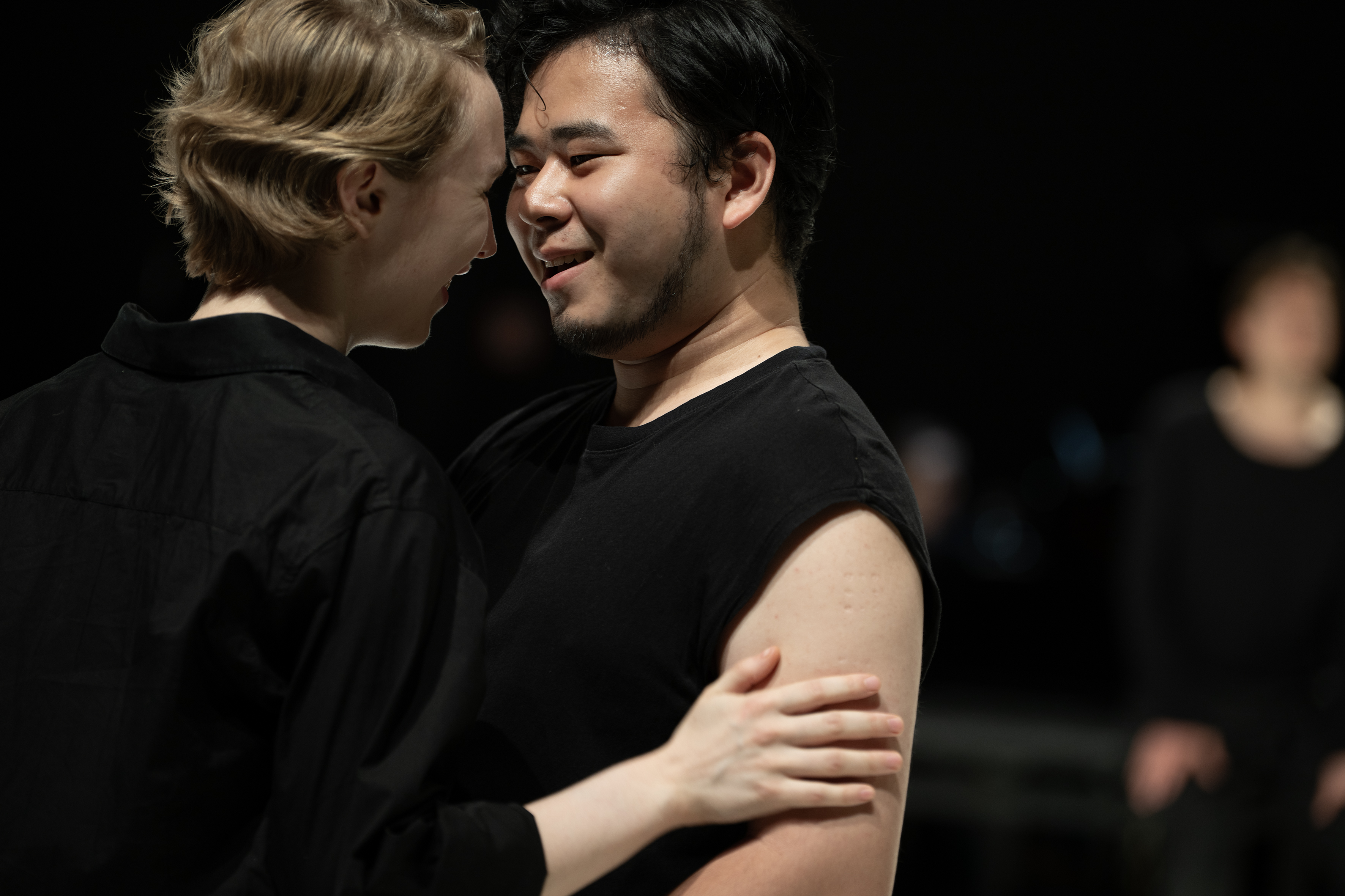 Szenenfoto: Zwei Personen in schwarzer Kleidung (Madeleine Shari Wulff, Tatsuki Sakamoto) umarmen sich und lächeln sich an