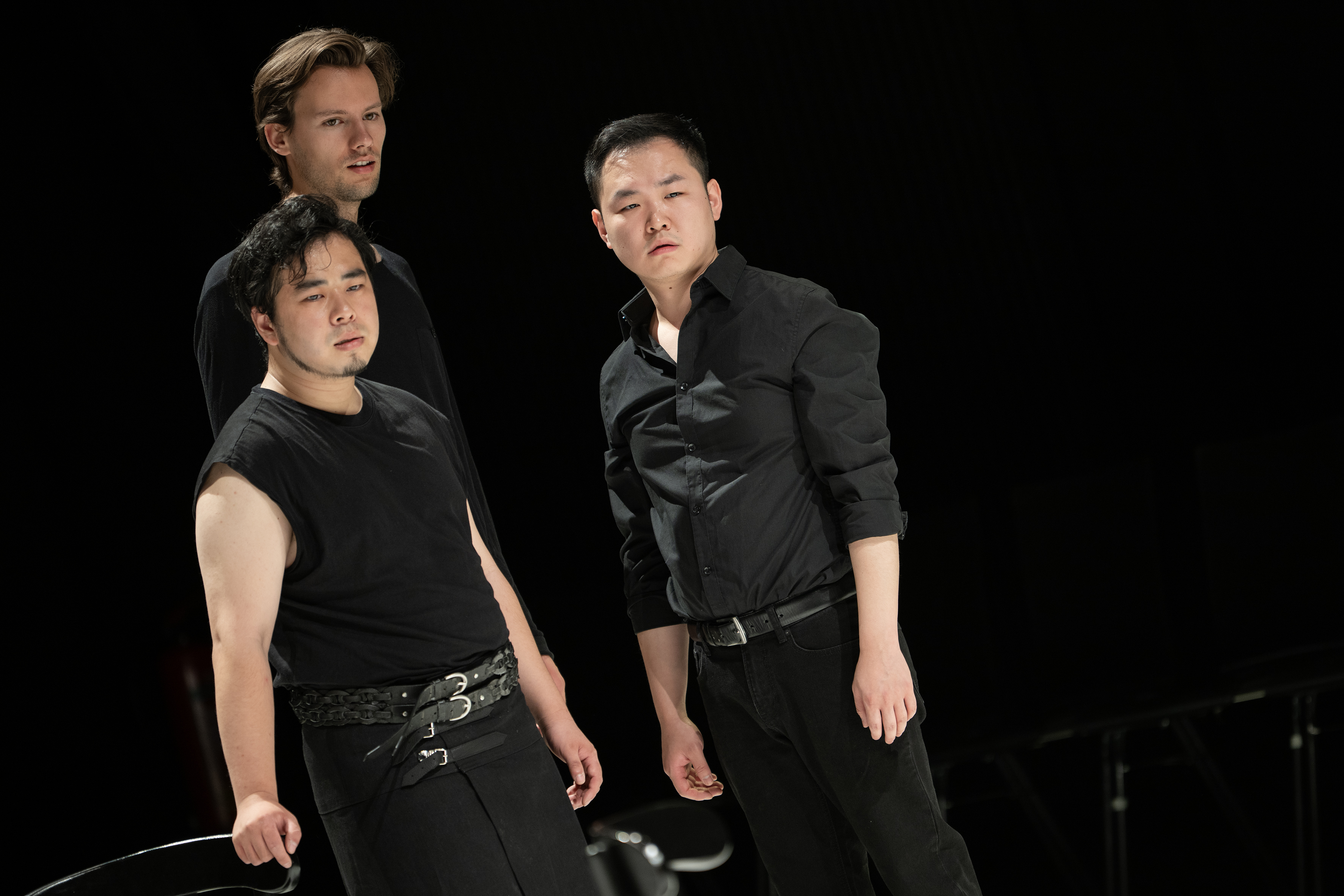 Szenenfoto: Drei Männer (Tatsuki Sakamoto, Luis Weidlich, Haozhou Hu) in schwarzer Kleidung stehen vor dunklem Hintergrund und blicken nach vorn