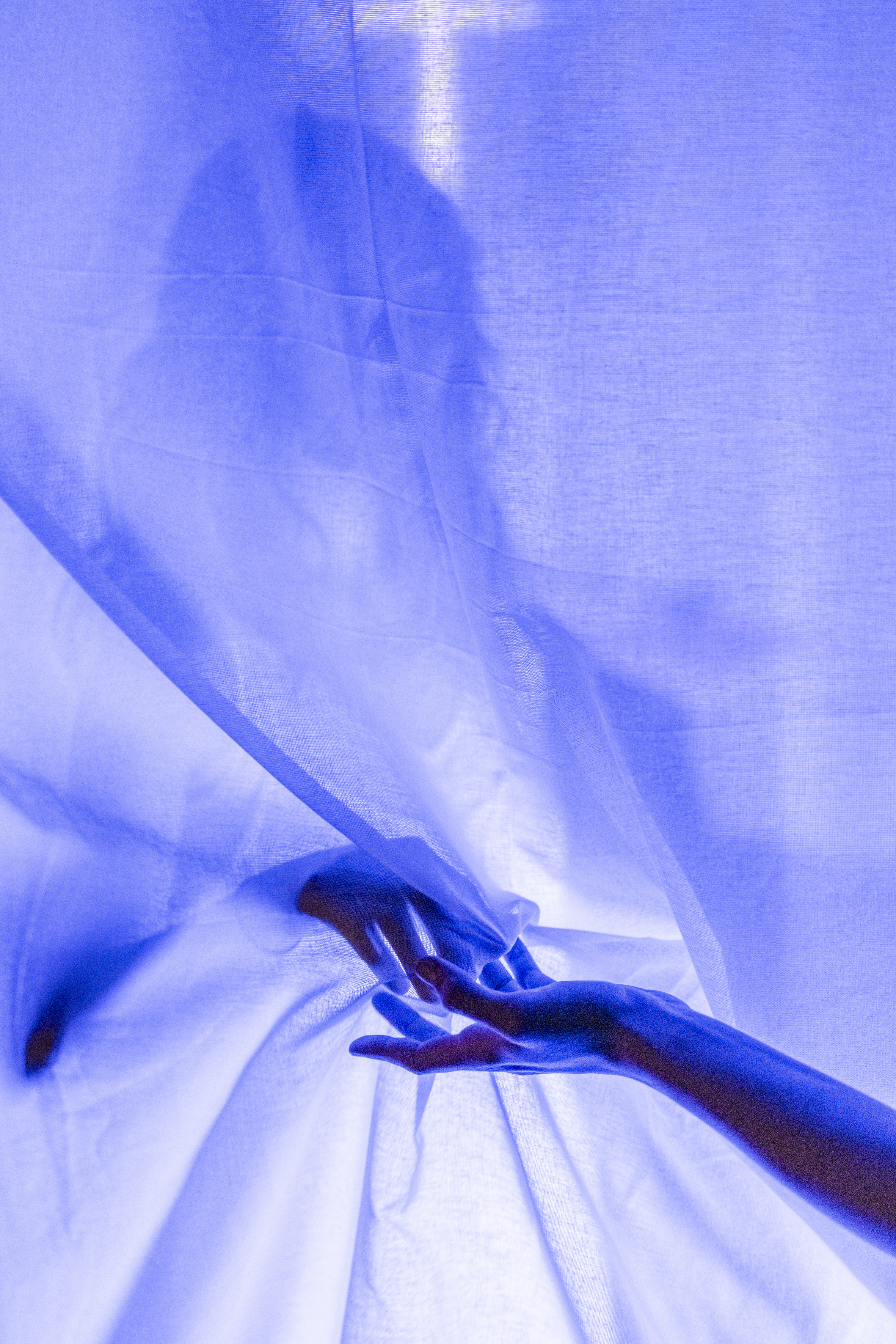 Eine Hand greift durch einen halbtransparenten Vorhang, hinter dem eine verschwommene Silhouette einer Person zu sehen ist