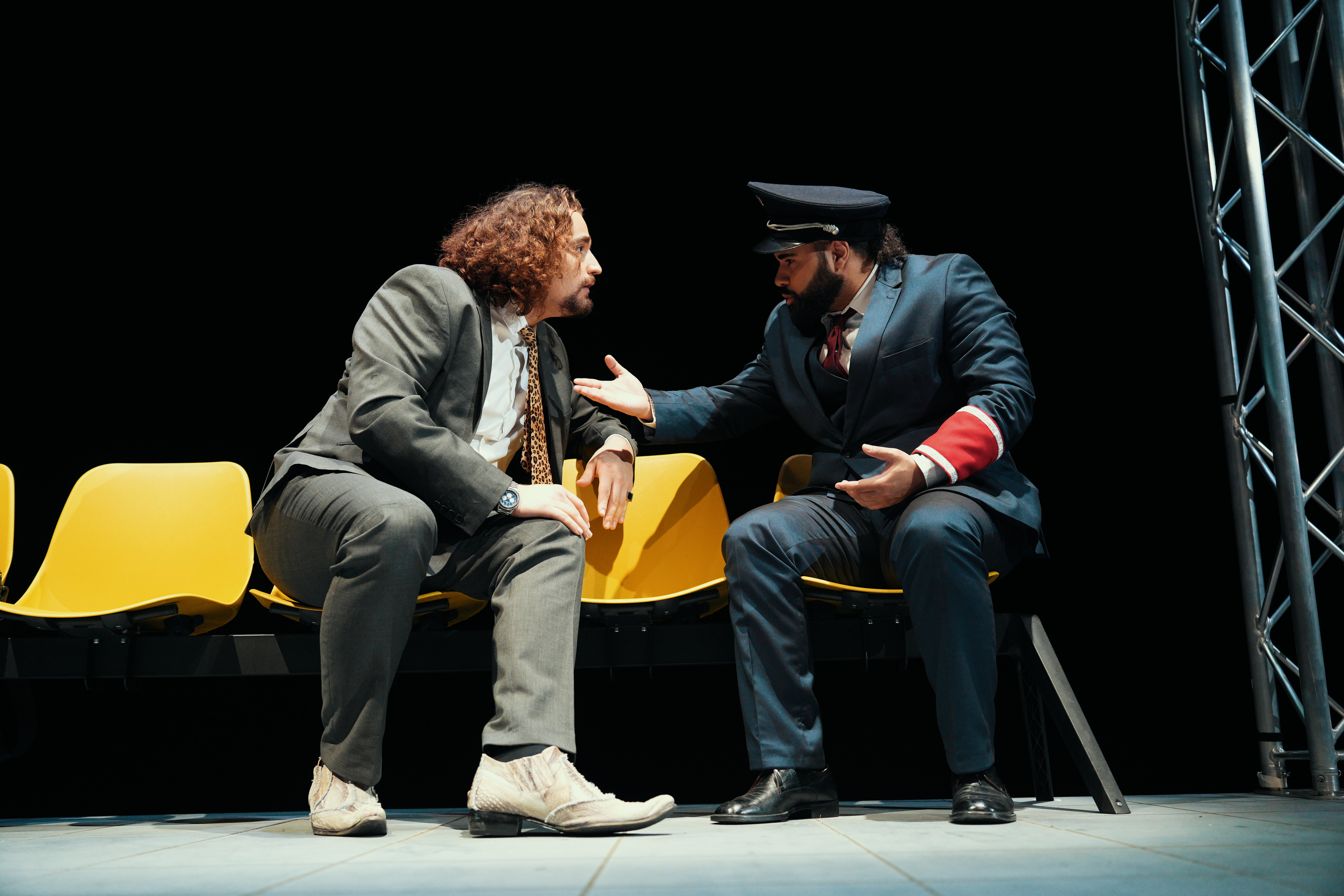 Zwei Männer sitzen auf einer Wartebank und diskutieren.