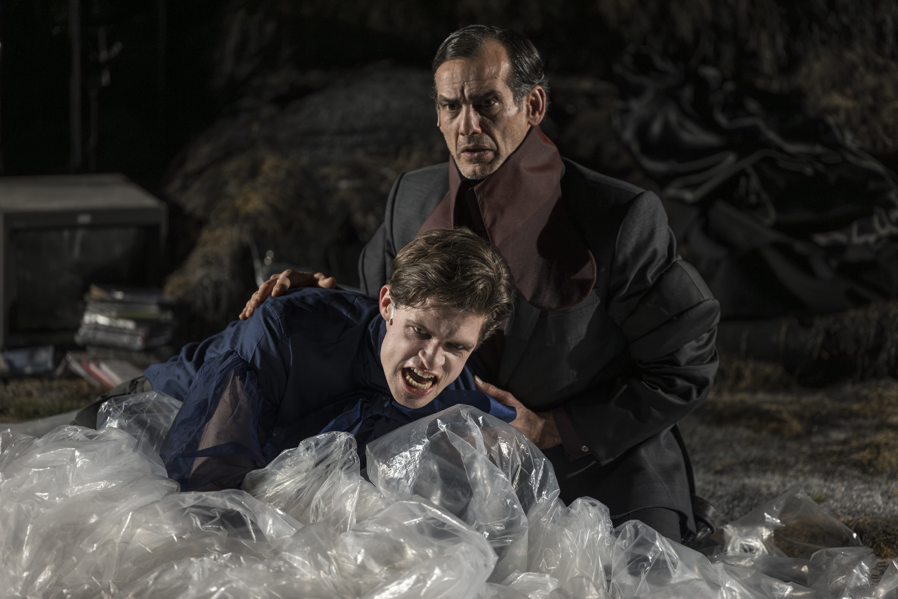 Ein Mann hält einen mit verzerrtem Gesicht und auf dem mit Folie bedeckten Boden liegenden Mann fest