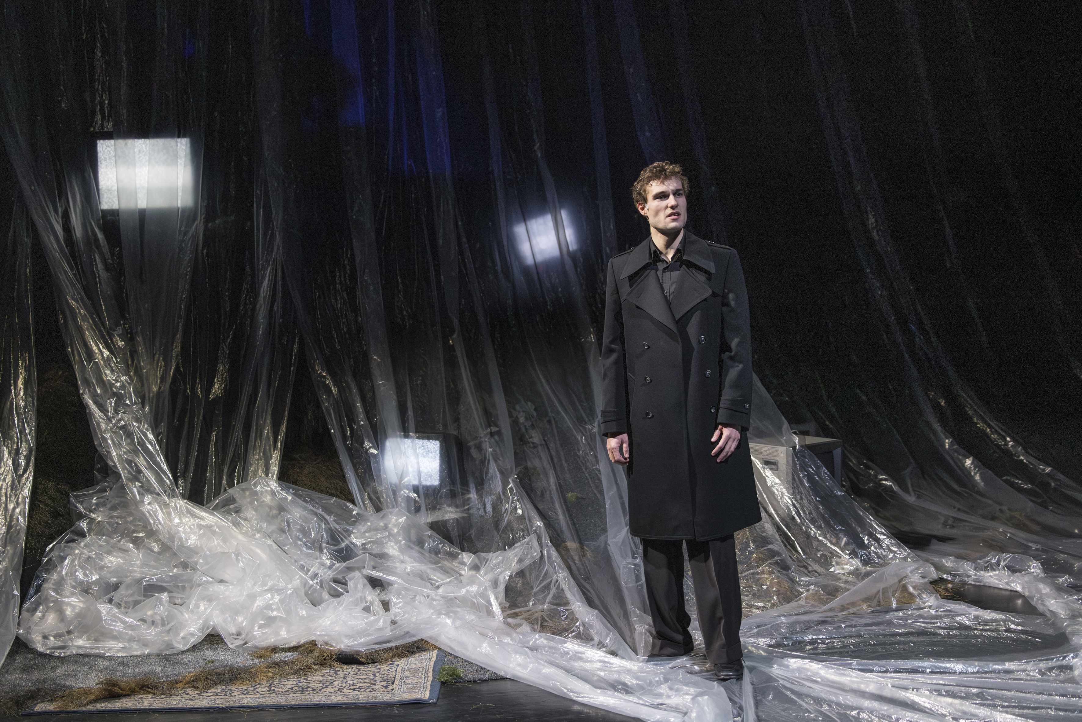 Ein Mann im Mantel steht vor Folienvorhängen, hinter denen sich leuchtende Bildschirme befinden