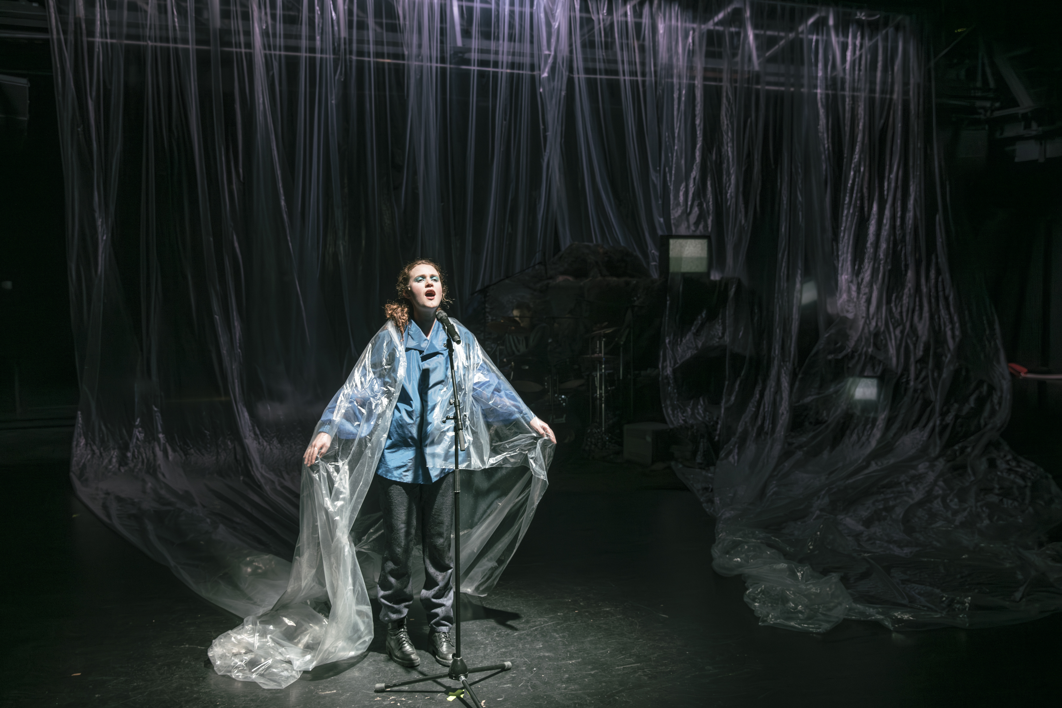 Eine Person steht, von Folie umschlungen, vor einem Mikrofon