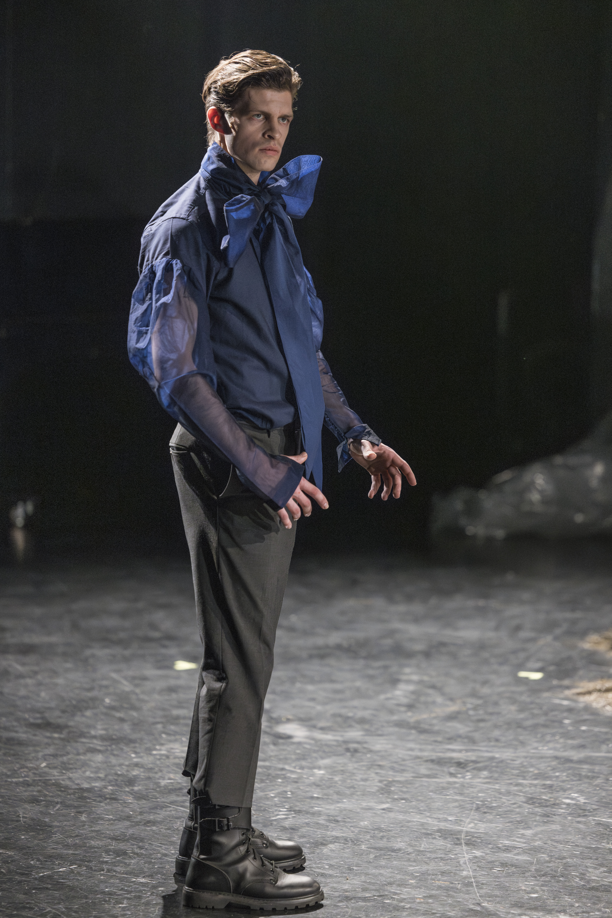 Ein Mann in Hemd mit großer Schleife steht aufrecht mit präzisem Blick nach rechts