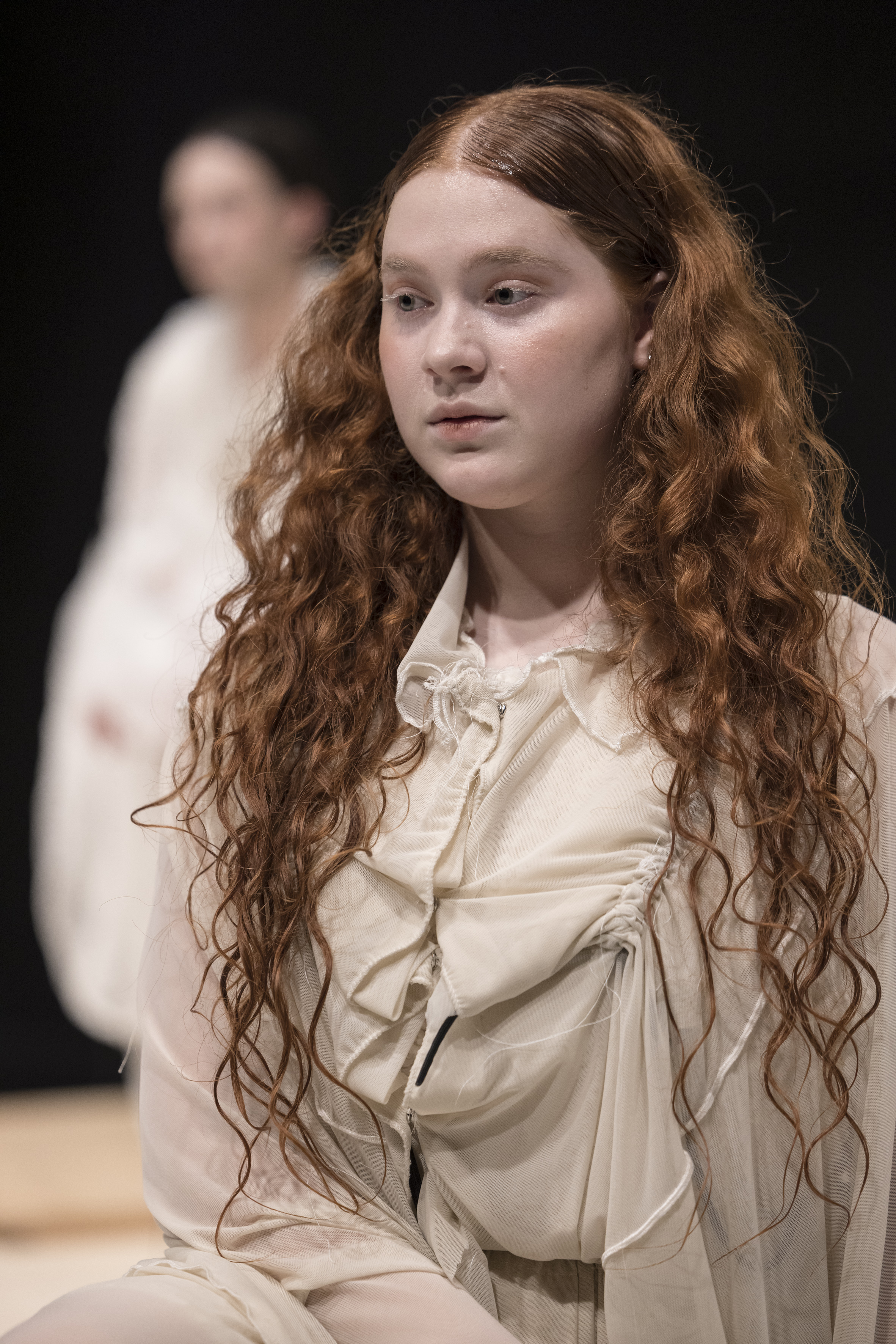 Person mit langen, lockigen Haaren trägt ein helles Gewand