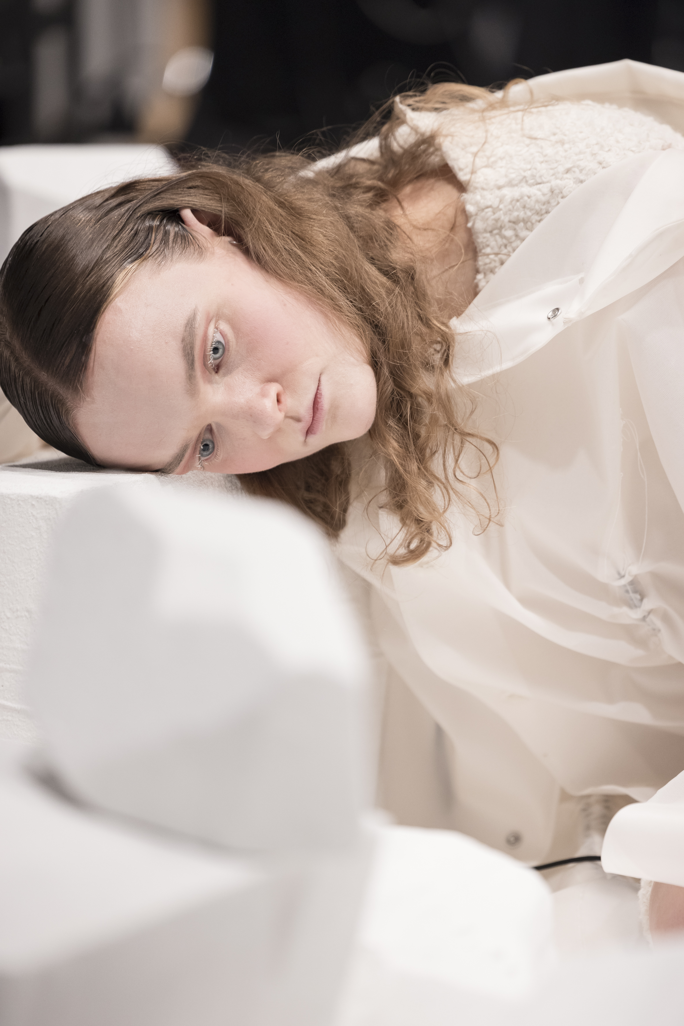 Person mit langen Haaren lehnt seitlich mit dem Kopf auf einer weißen Oberfläche