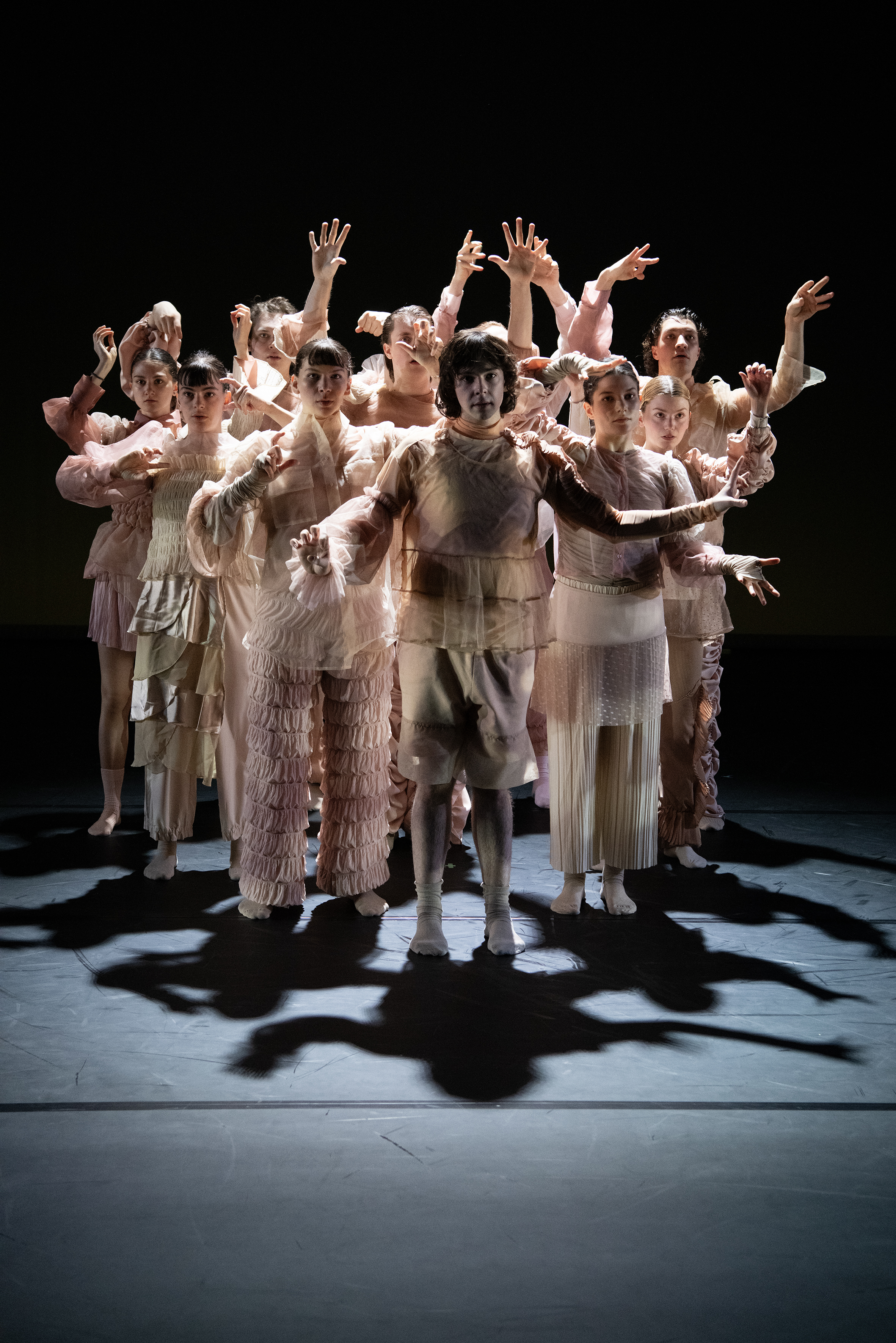 Das Ensemble steht geschlossen als Gruppe im Spotlight, verschiedene Handposen