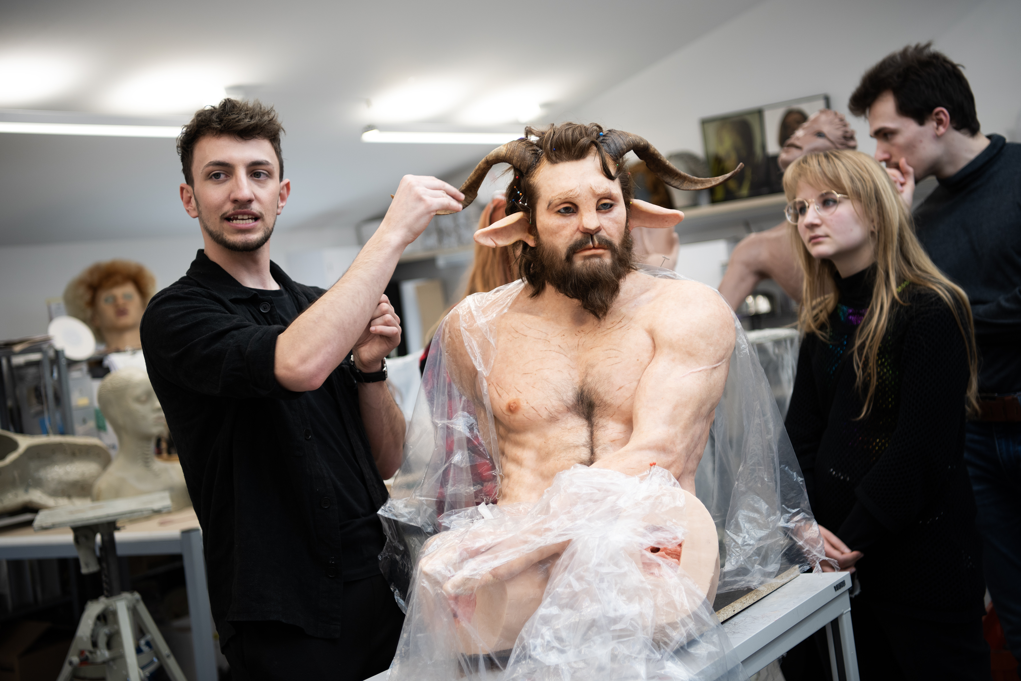 Studierende zeigen eine lebensecht aussehende Maskenarbeit, die einen Menschen mit Hörnern zeigt