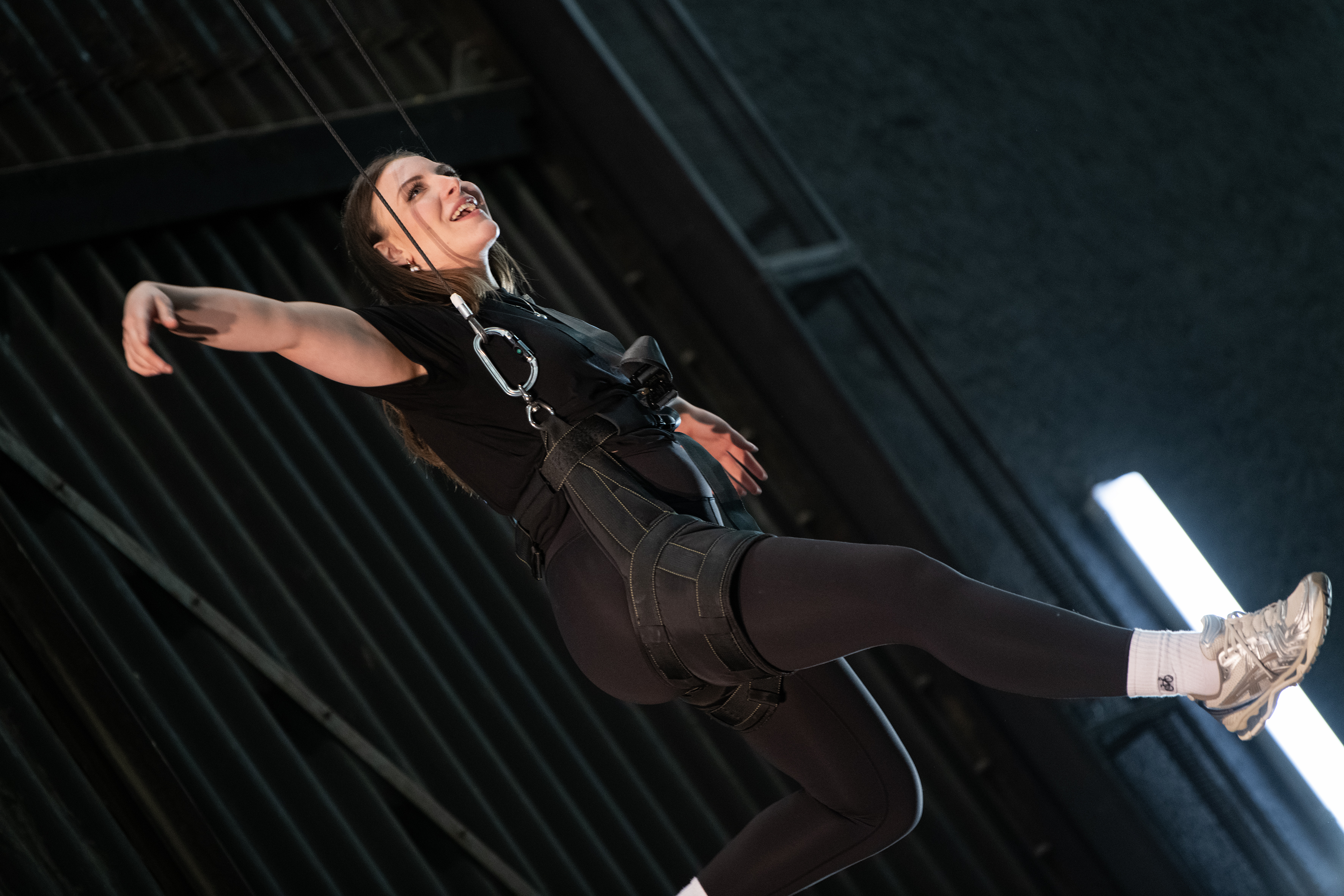 Eine Studierende im Fluggeschirr in der Luft mit ausgebreiteten Armen