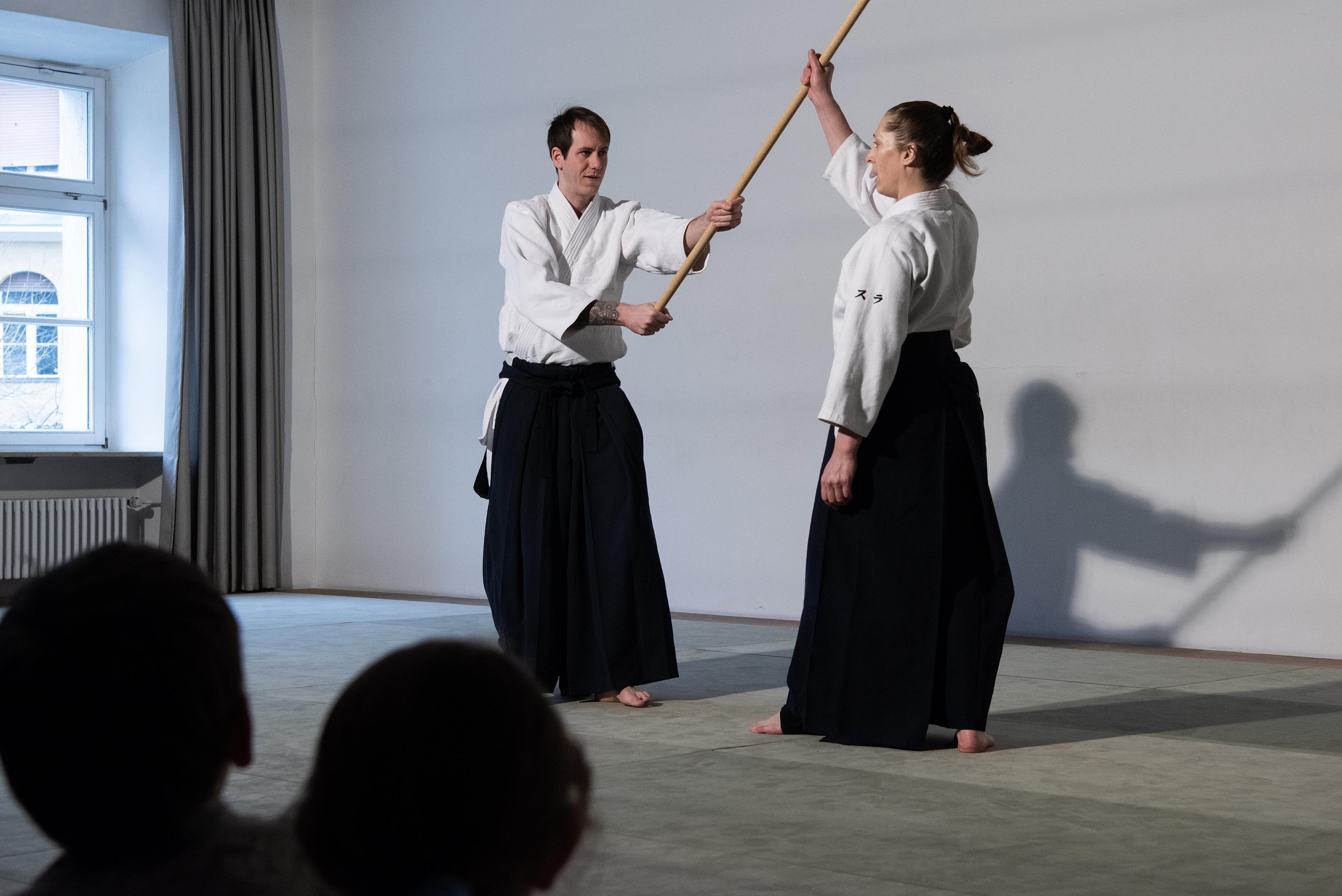 Ein Mann hält einen Aikido-Kampfstab, ihm gegenüber steht eine Frau, die den Stab festhält