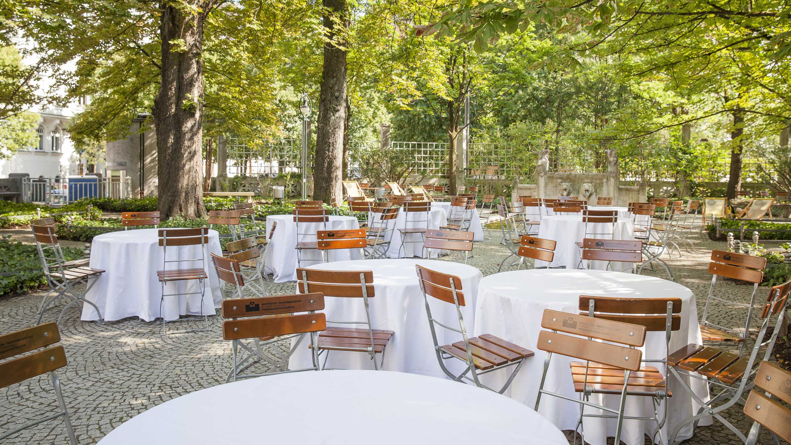 Mehrere Tische und Stühle unter großen Bäumen