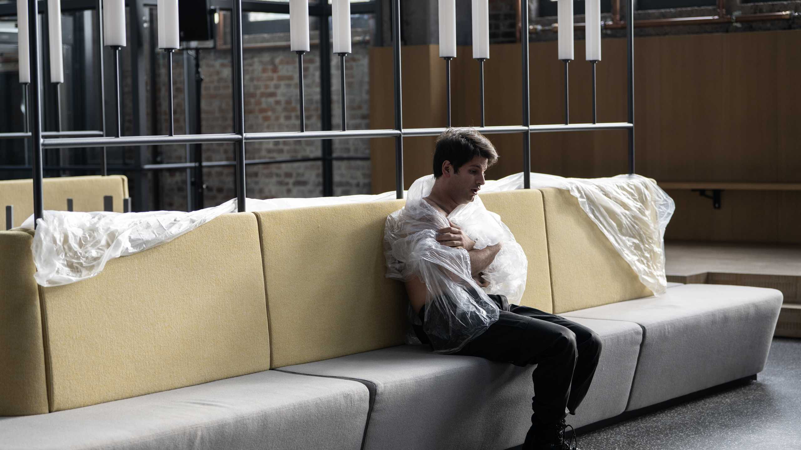 Henrique Lencastre in der Rolle des Lazarus sitzt in Folie gewickelt allein auf einer Bank im Atrium vom Bergson Kunstkraftwerk