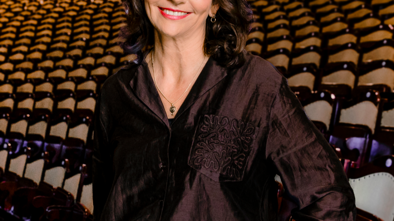 Foto von Amélie Niermeyer mit dunklem Hemd, steht lächelnd im großen, leeren Prinzregententheater, hinter ihr viele Sitzreihen